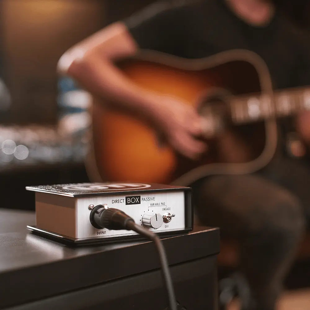 Warm audio Direct box with audio cable on a stand, with a person playing an acoustic guitar 